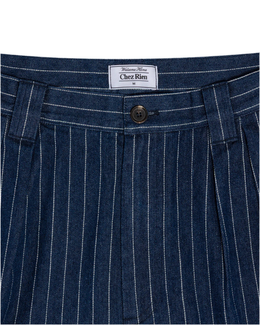 Close-up of indigo pinstripe shorts with a ‘Chez Rien’ brand label on a white background