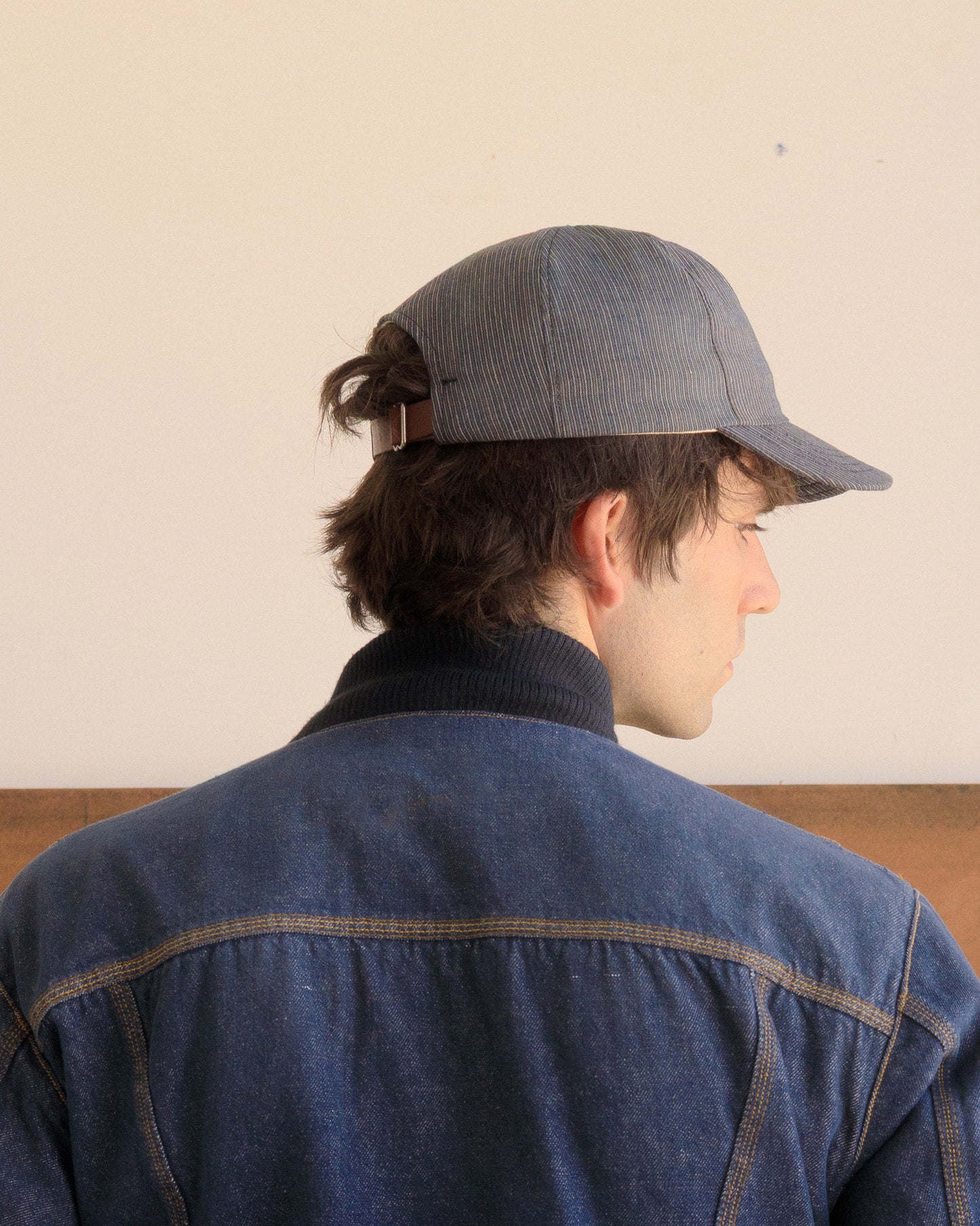 Back of man wearing a Blue Thin Stripe Warden Cap and denim jacket against a plain background