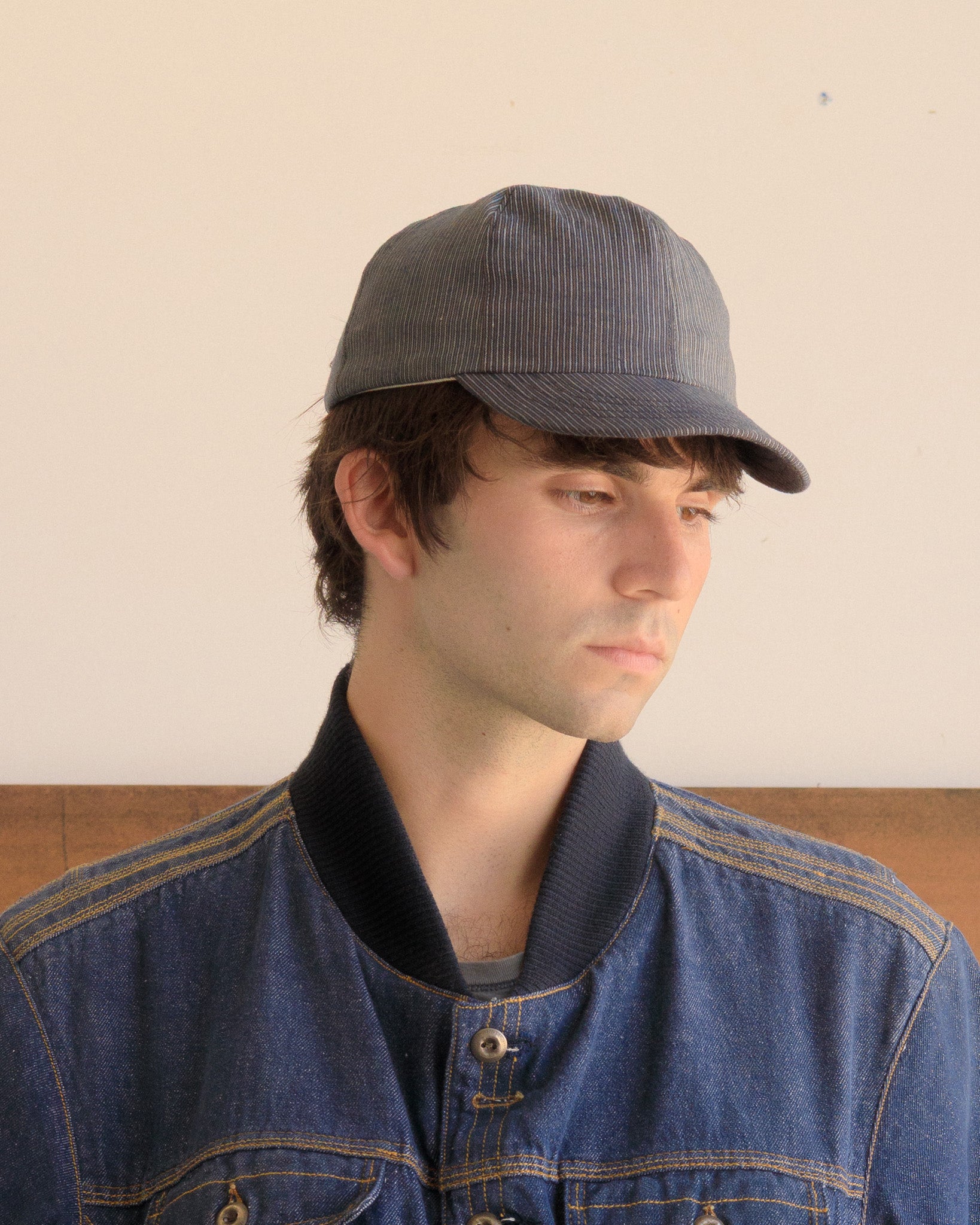 Man wearing a Blue Thin Stripe Warden Cap and denim jacket against a plain background